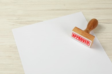 Image of Wooden stamp with word Approved and blank sheet of paper on table