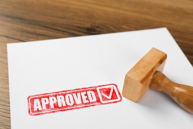 Image of Sheet of paper with red stamp Approved and wooden stamp on table, closeup