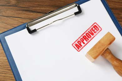 Image of Sheet of paper with red stamp Approved and wooden stamp on table, closeup
