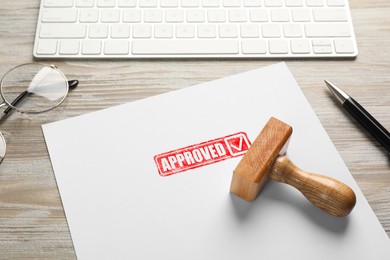 Image of Sheet of paper with red stamp Approved and wooden stamp on table. Workplace with computer keyboard