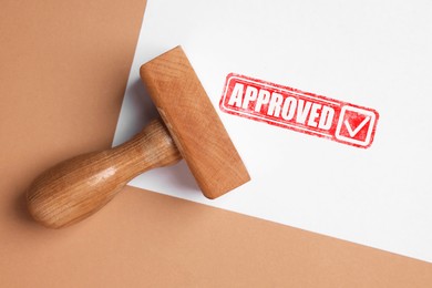 Image of Sheet of paper with red stamp Approved and wooden stamp on pale brown background