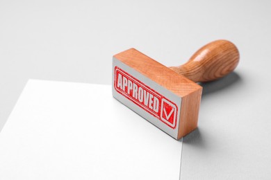 Image of Wooden stamp with word Approved and blank sheet of paper on table