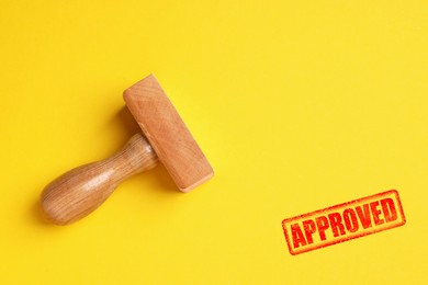 Image of Red stamp Approved and wooden stamp on yellow background, top view