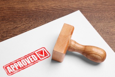 Image of Sheet of paper with red stamp Approved and wooden stamp on table