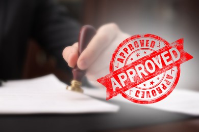 Image of Man stamping document at table and red stamp Approved