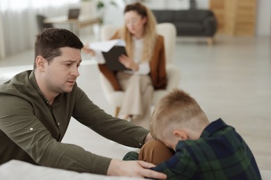 Photo of Father and son having consultation with psychologist in office, selective focus