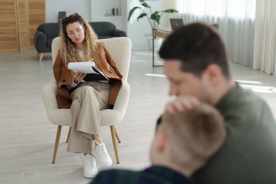 Photo of Father and son having consultation with psychologist in office, selective focus