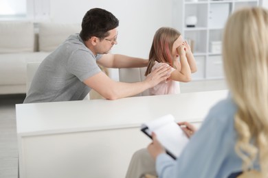 Photo of Father and daughter having consultation with psychologist in office, selective focus