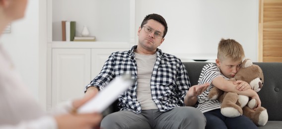 Photo of Father and son having consultation with psychologist in office, selective focus