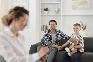 Photo of Happy father and son having consultation with psychologist in office, selective focus