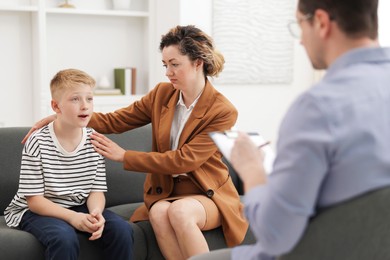 Photo of Mother and son having consultation with psychologist in office, selective focus