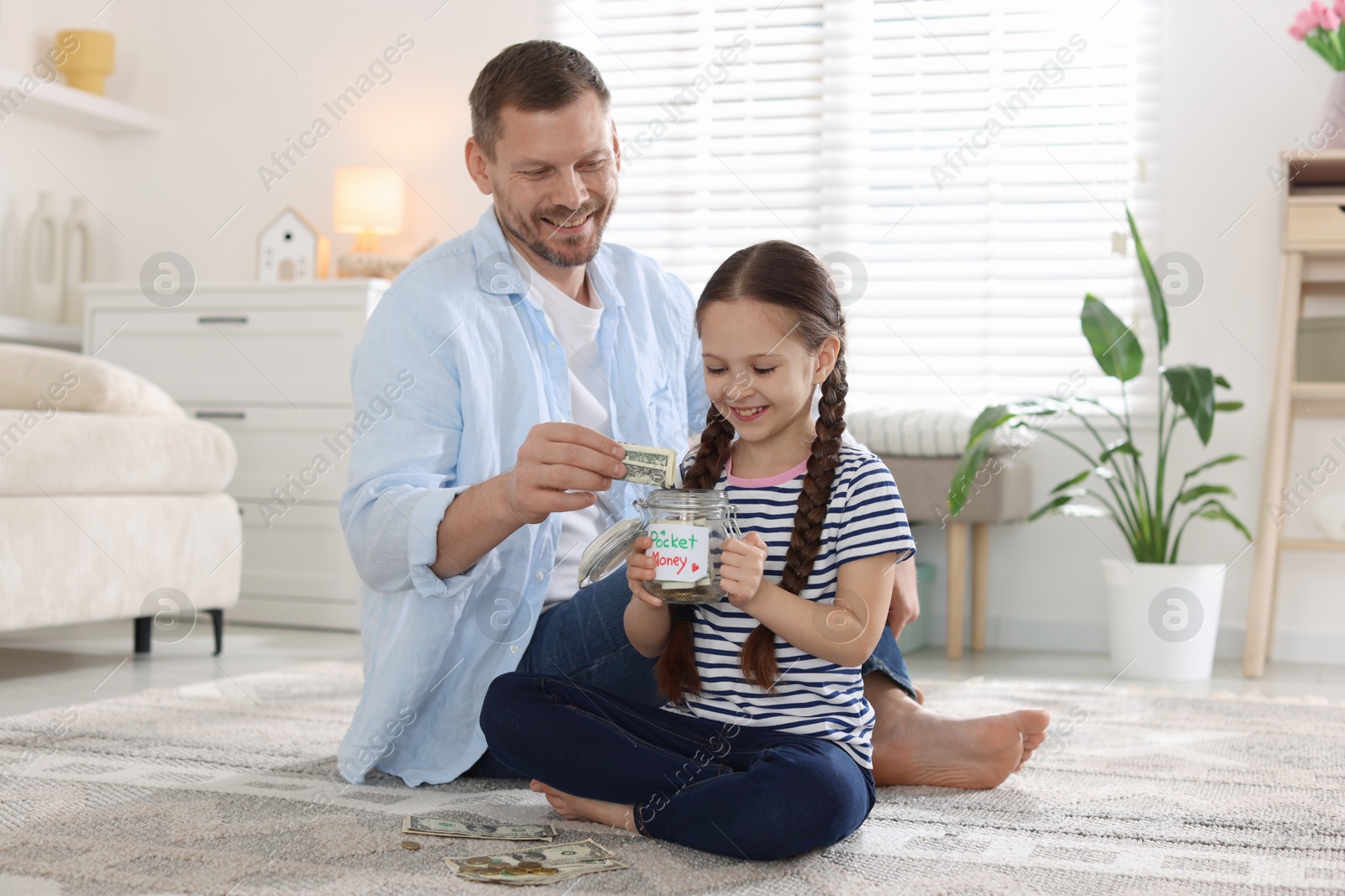 Father and daughter putting pocket money into jar at home Photo of Father and daughter putting pocket money into jar at home