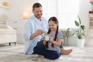 Photo of Father and daughter putting pocket money into jar at home