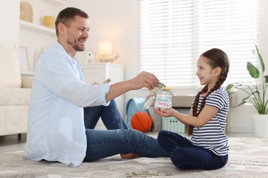 Photo of Father and daughter putting pocket money into jar at home