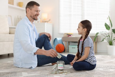 Photo of Father and daughter putting pocket money into jar at home