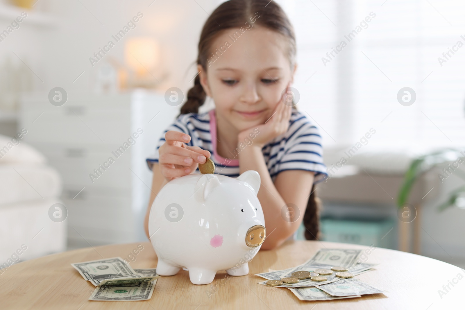 Girl putting her pocket money into piggybank at table indoors, selective focus Photo of Girl putting her pocket money into piggybank at table indoors, selective focus