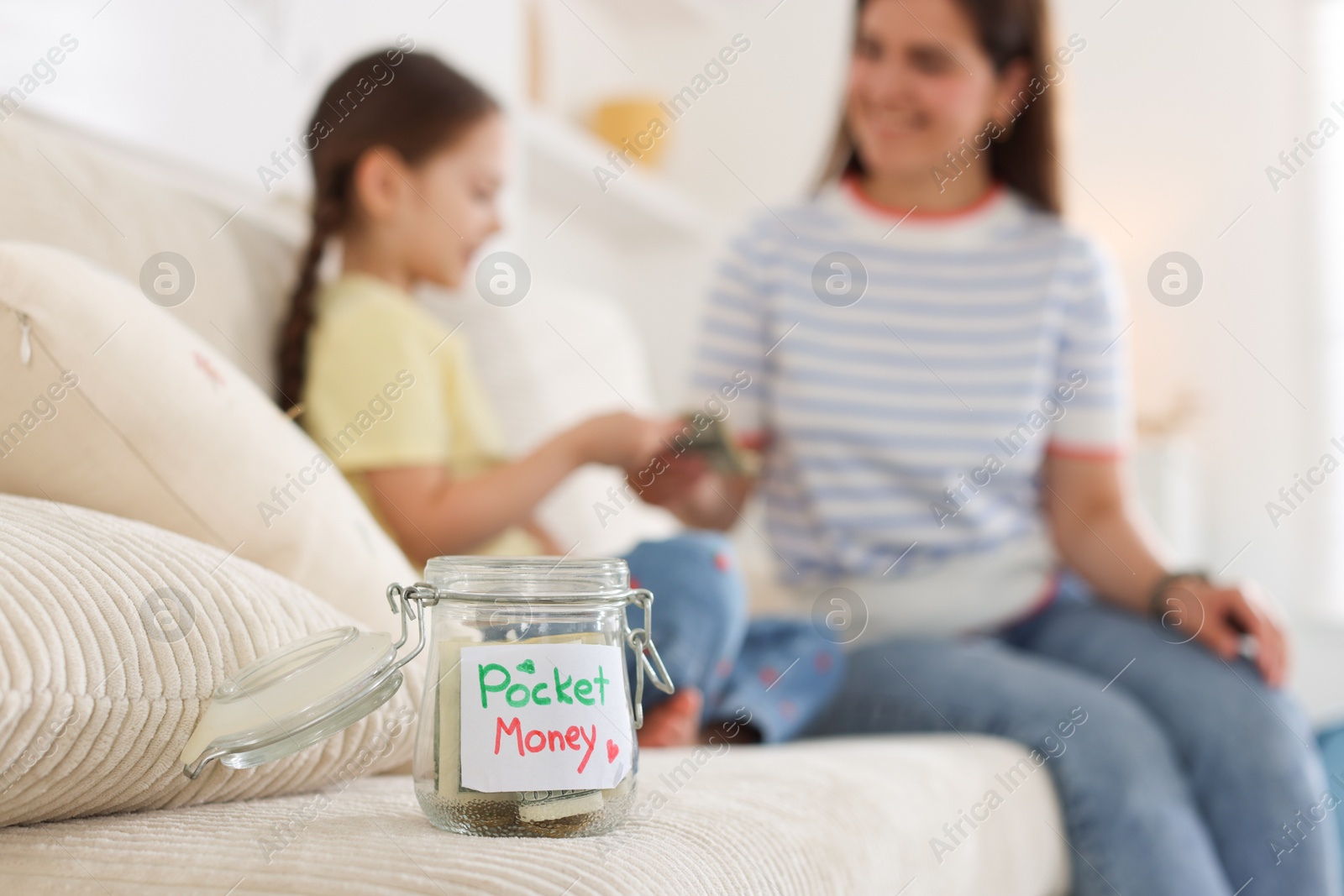 Jar with pocket money, mother and daughter on sofa at home, selective focus Photo of Jar with pocket money, mother and daughter on sofa at home, selective focus