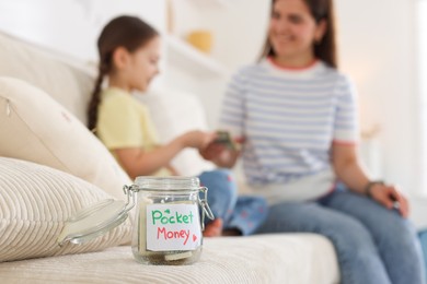 Photo of Jar with pocket money, mother and daughter on sofa at home, selective focus
