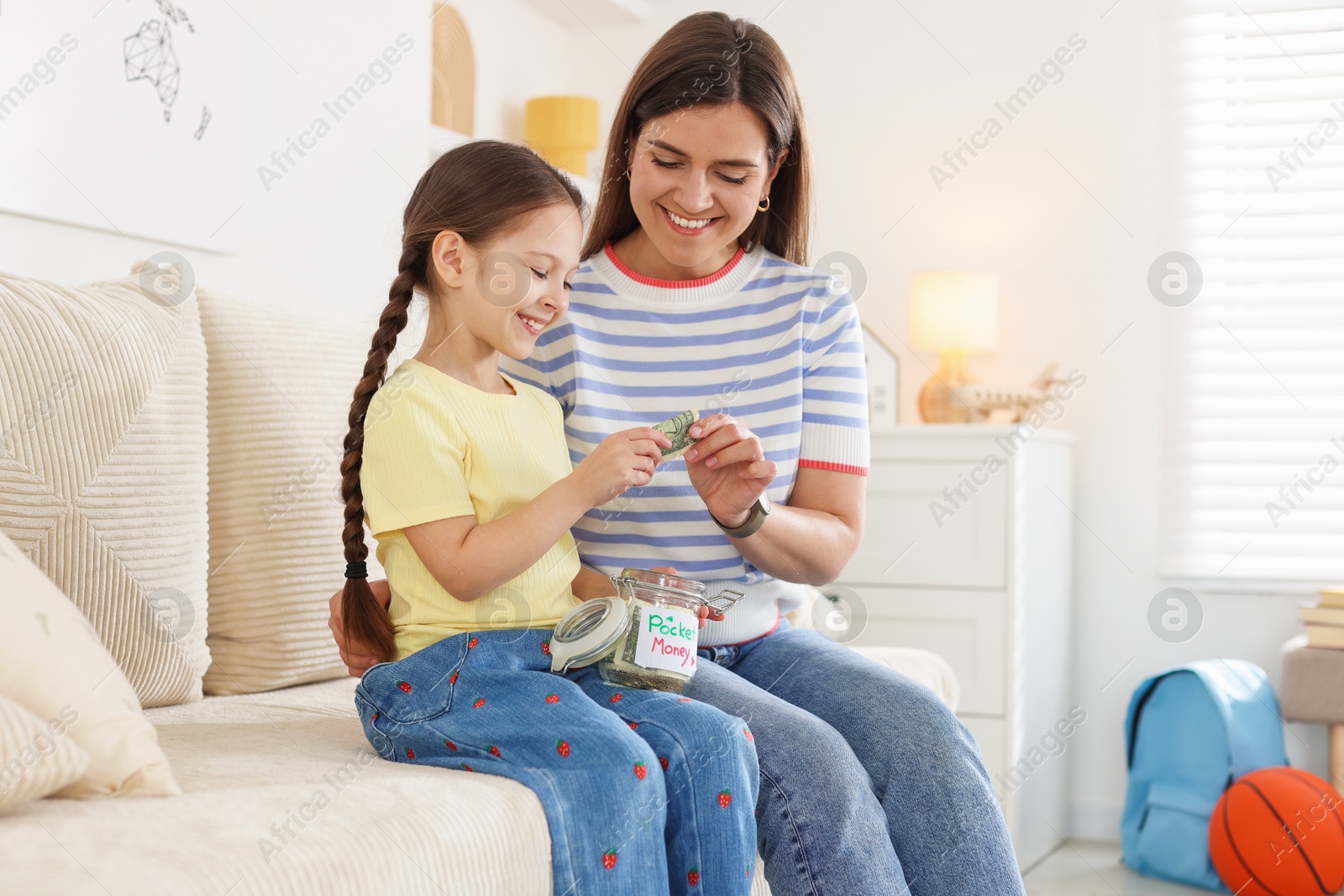 Mother giving her daughter pocket money on sofa at home Photo of Mother giving her daughter pocket money on sofa at home