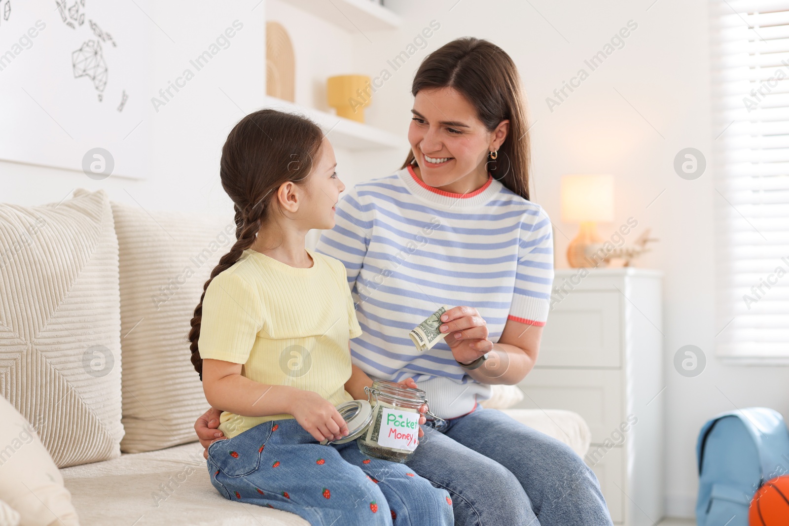 Mother giving her daughter pocket money on sofa at home Photo of Mother giving her daughter pocket money on sofa at home