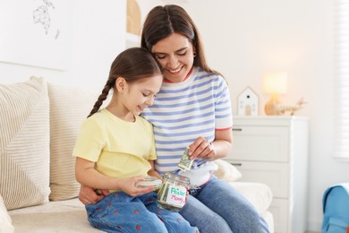 Photo of Mother giving her daughter pocket money on sofa at home