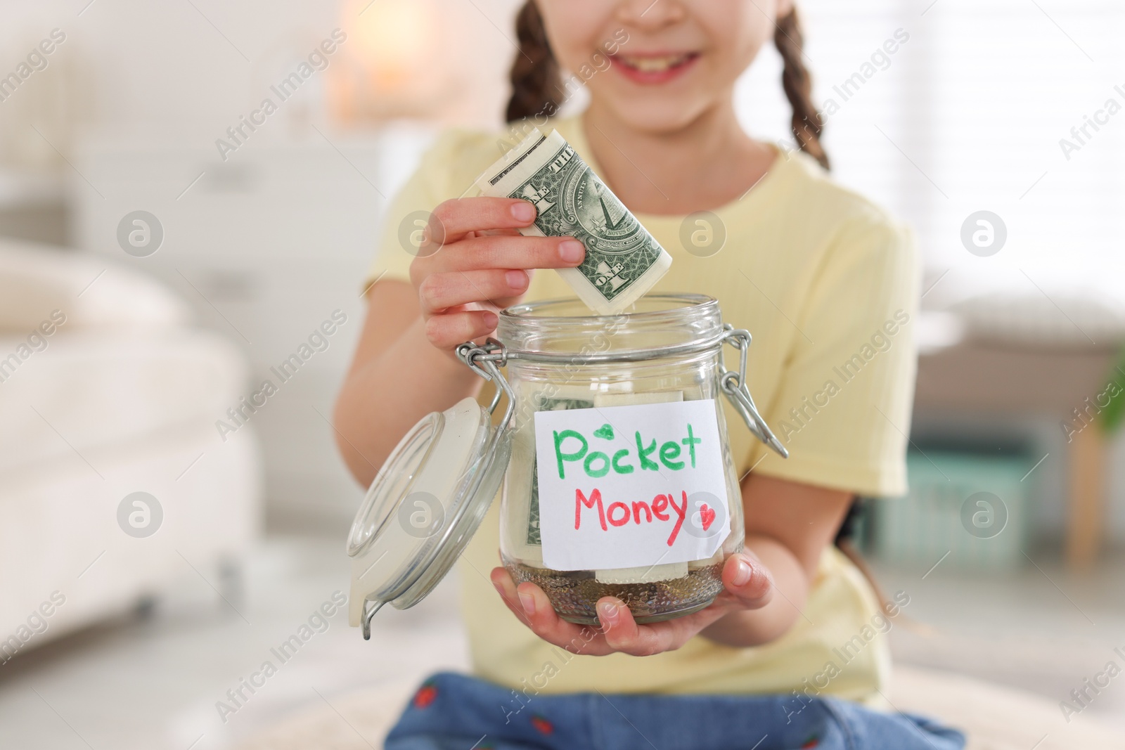 Girl putting her pocket money into jar at home, closeup Photo of Girl putting her pocket money into jar at home, closeup