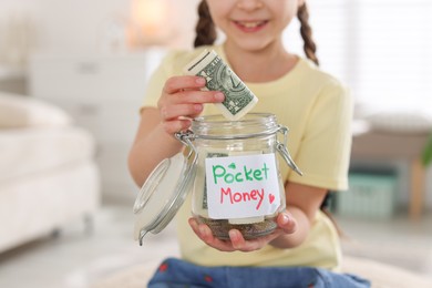 Photo of Girl putting her pocket money into jar at home, closeup