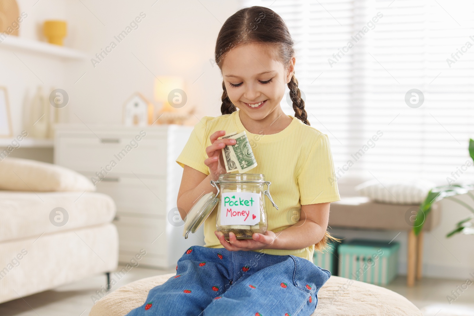 Girl putting her pocket money into jar at home Photo of Girl putting her pocket money into jar at home