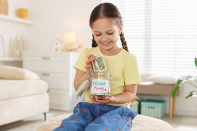Photo of Girl putting her pocket money into jar at home