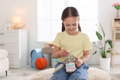 Photo of Girl putting her pocket money into jar at home