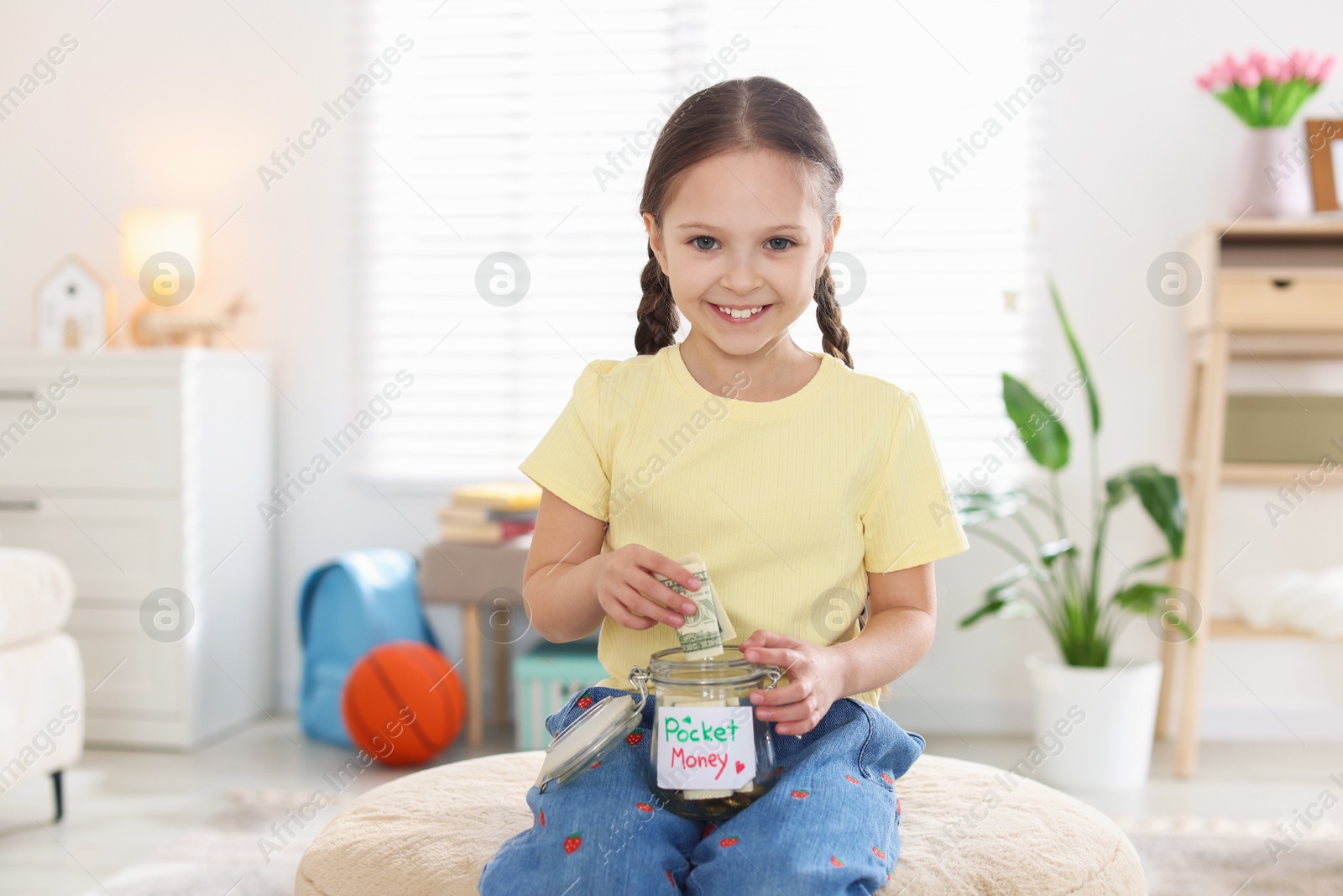 Girl putting her pocket money into jar at home Photo of Girl putting her pocket money into jar at home
