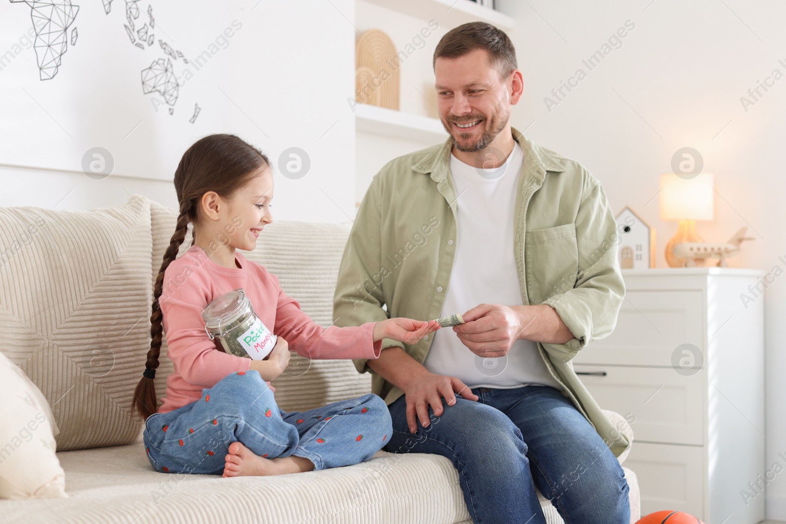 Father giving his daughter pocket money on sofa at home Photo of Father giving his daughter pocket money on sofa at home