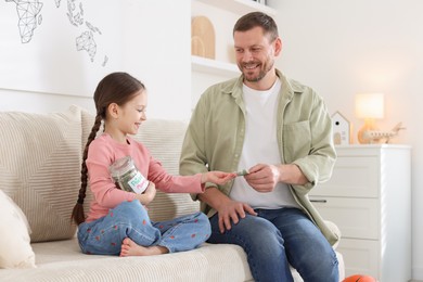 Photo of Father giving his daughter pocket money on sofa at home