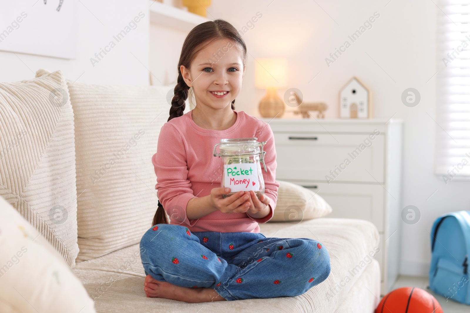 Girl with jar of pocket money on sofa at home Photo of Girl with jar of pocket money on sofa at home