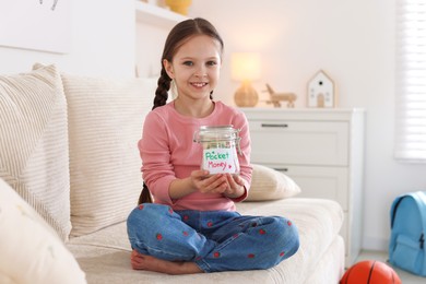 Photo of Girl with jar of pocket money on sofa at home