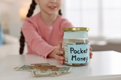 Photo of Girl with jar of pocket money at table indoors, closeup