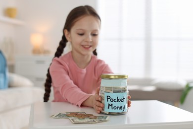 Photo of Girl with jar of pocket money at table indoors. Space for text