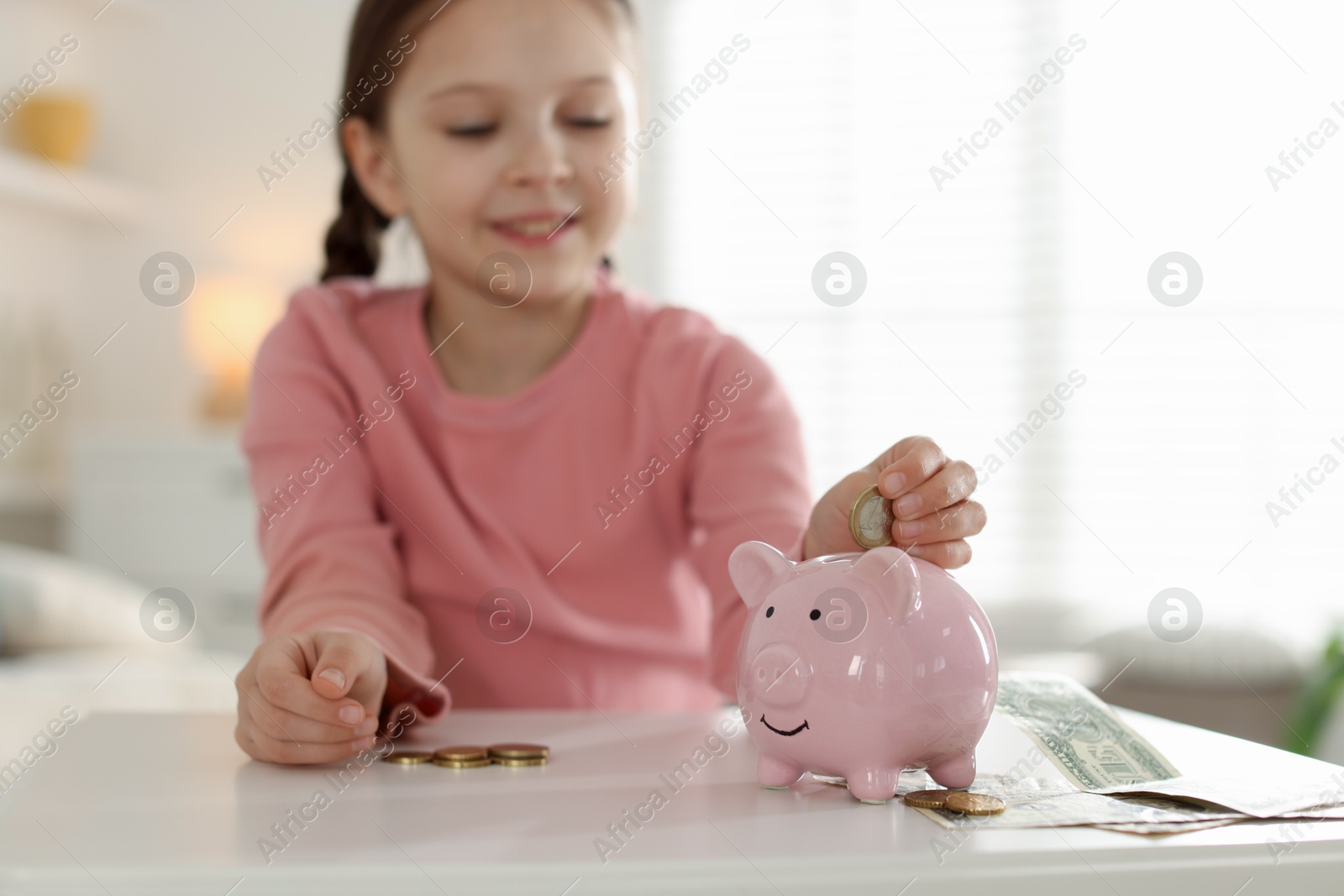 Girl putting her pocket money into piggybank at table indoors, selective focus Photo of Girl putting her pocket money into piggybank at table indoors, selective focus