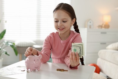 Photo of Girl putting her pocket money into piggybank at table indoors