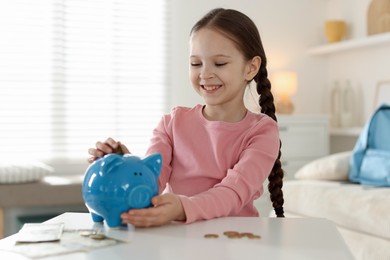 Photo of Girl putting her pocket money into piggybank at table indoors