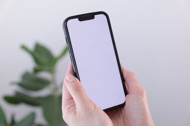 Photo of Woman holding smartphone with blank screen on blurred background, closeup. Mockup for design