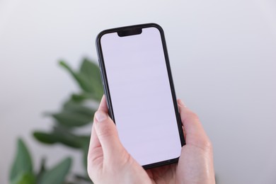 Photo of Woman holding smartphone with blank screen on blurred background, closeup. Mockup for design