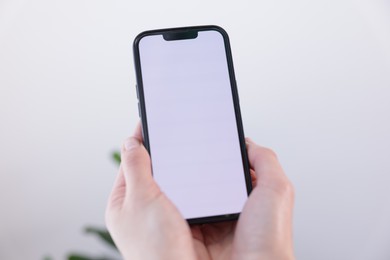 Photo of Woman holding smartphone with blank screen on blurred background, closeup. Mockup for design
