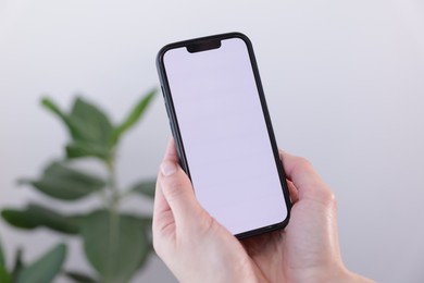 Photo of Woman holding smartphone with blank screen on blurred background, closeup. Mockup for design