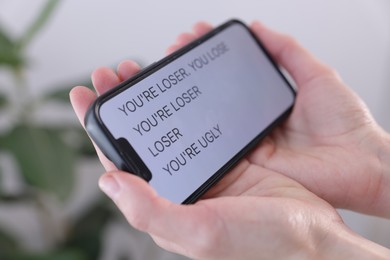 Photo of Cyber bullying. Woman holding smartphone with insults on blurred background, closeup