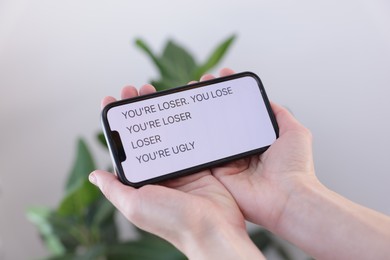 Photo of Cyber bullying. Woman holding smartphone with insults on blurred background, closeup