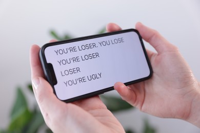 Photo of Cyber bullying. Woman holding smartphone with insults on blurred background, closeup