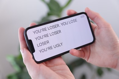 Photo of Cyber bullying. Woman holding smartphone with insults on blurred background, closeup