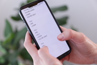 Photo of Cyber bullying. Woman holding smartphone with insults on blurred background, closeup