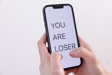 Photo of Cyber bullying. Woman holding smartphone with text You Are Loser on white background, closeup